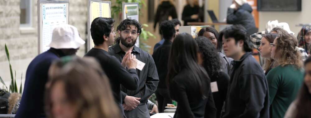 Students gather to watch a presenter in front of a board showcasing their products