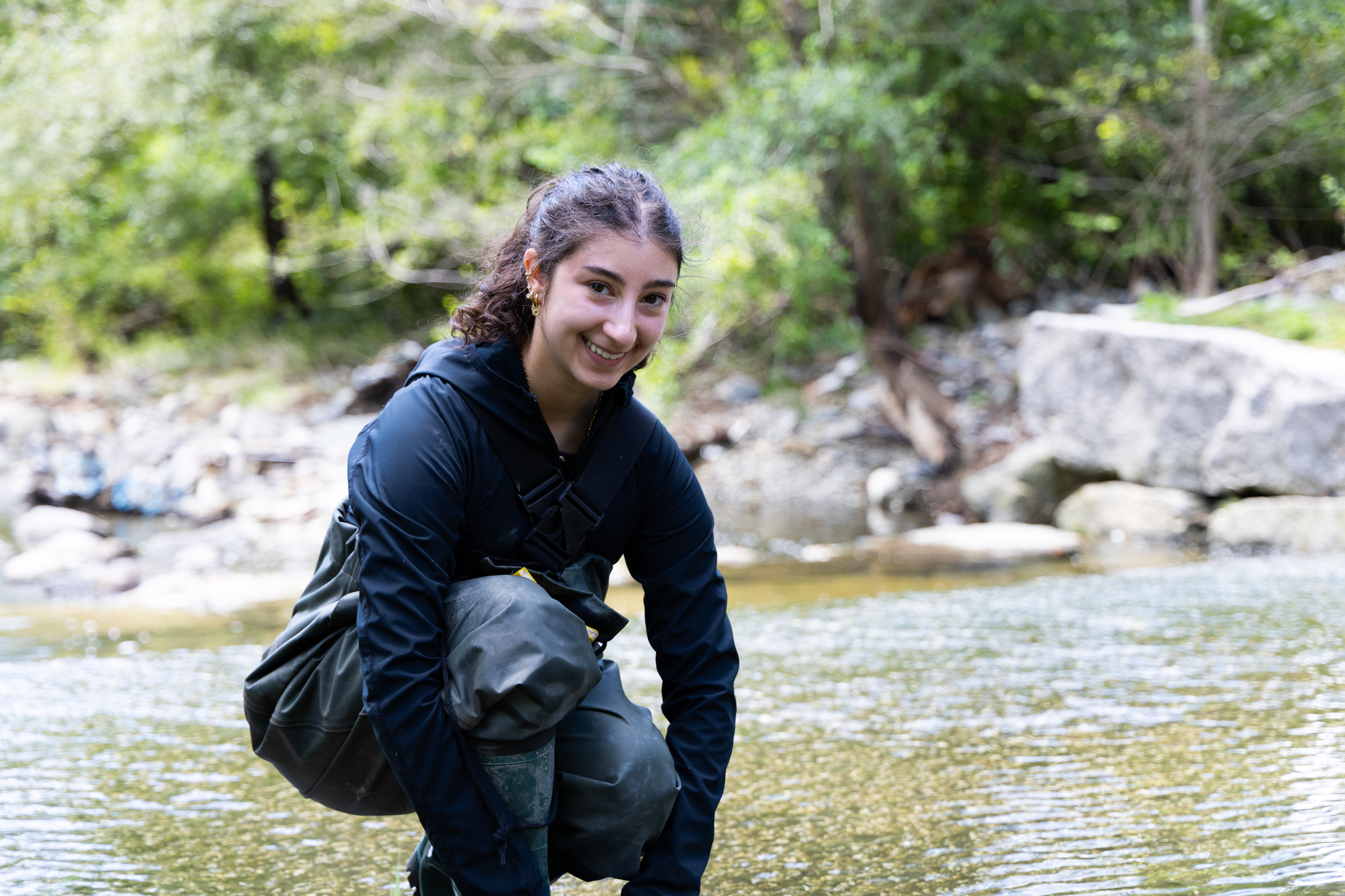 Student kneels in a shallow body of water to conduct research