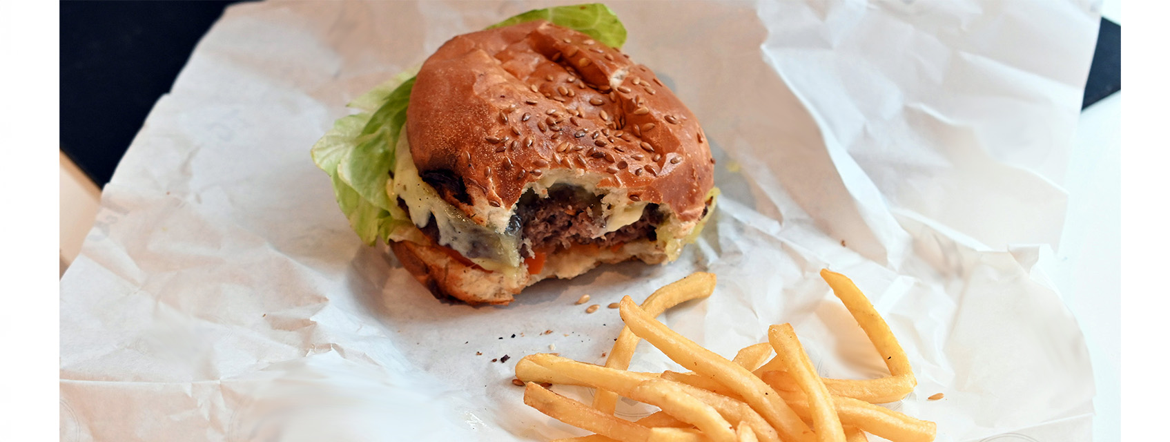 a fast food burger with a bite out of it on a white wrapper with fries in the foreground