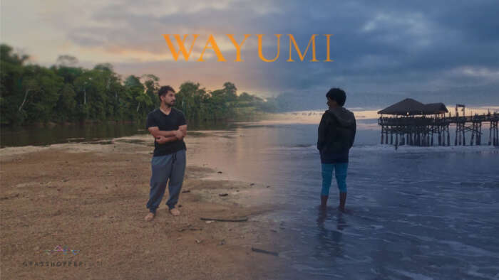 Wayumi. A man and a boy stand on a beach looking at each other. The boy is standing ankle deep in water and his half of the image has a blue overlay.