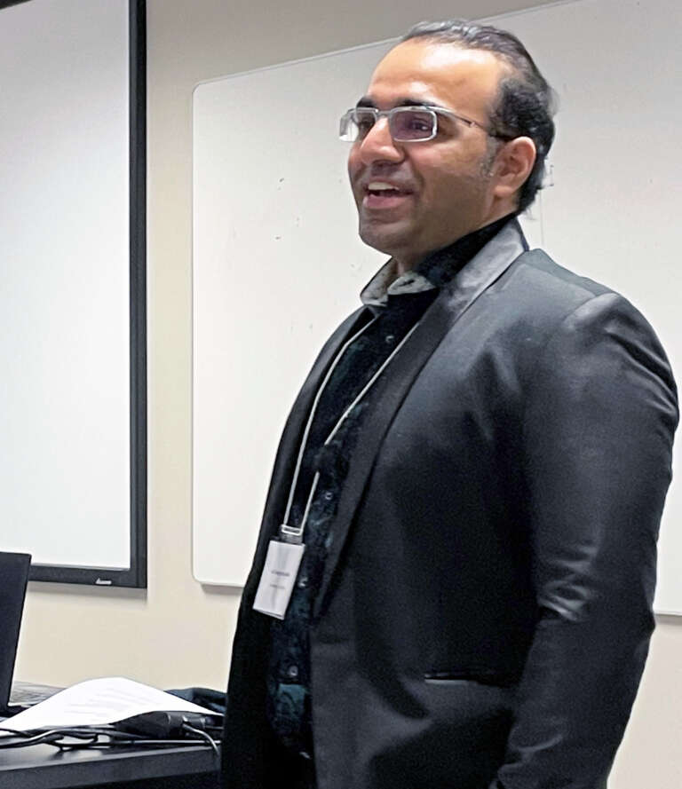 a person in a suit smiles while addressing a classroom