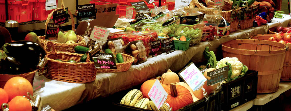 Several kinds of fruits and vegetables in baskets on tables with pricing signs
