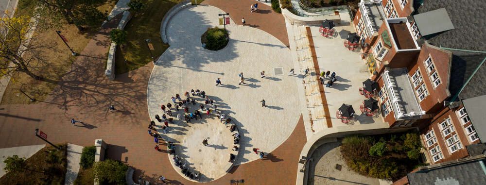 An aerial view of a red brick building and brick plaza with several people gathered in a circle