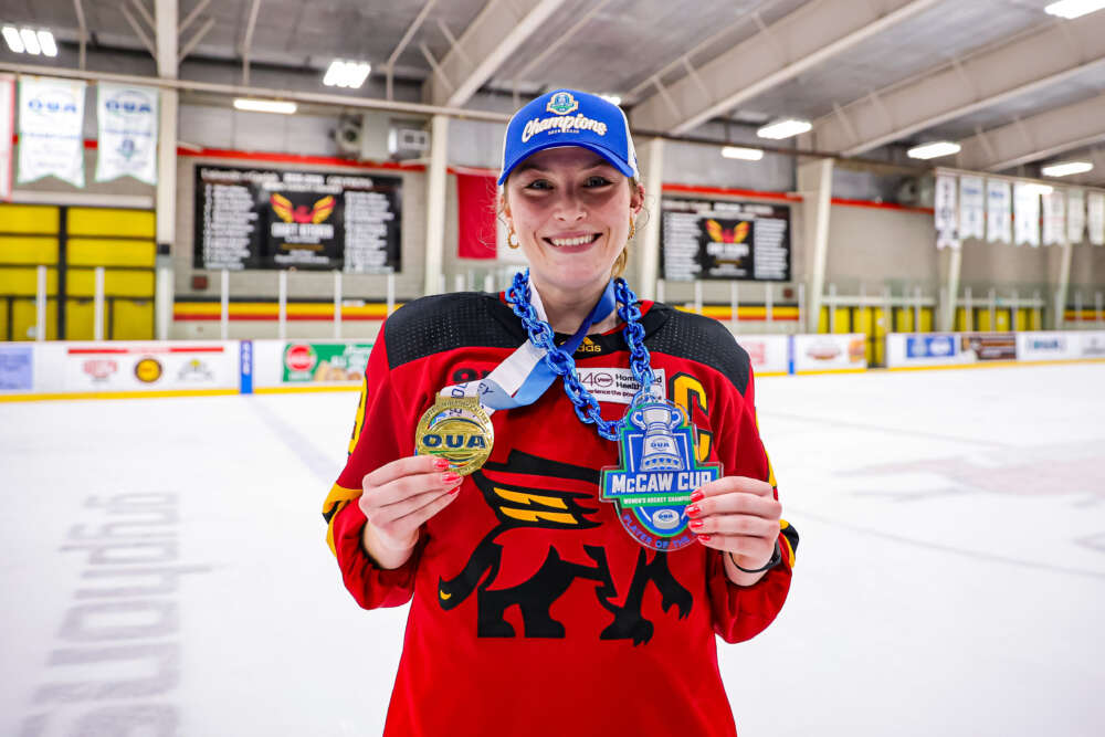 person in hockey jersey poses with medals that read oua and mccaw cup