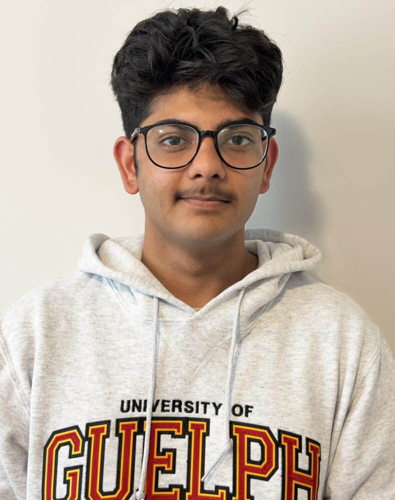 A student with short brown hair and black frame glasses wearing a grey U of G hoodie stands in front of a cream background looking into the camera.