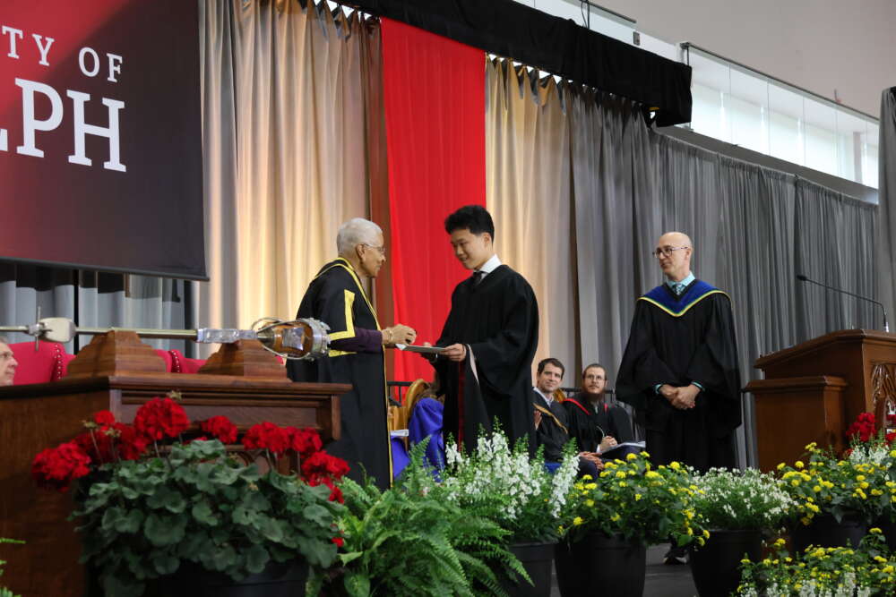 three people in convocation robes stand on a stage and one is handed a black box
