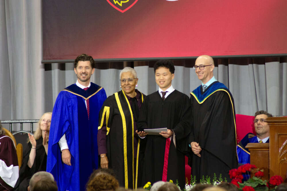 four people in robes stands on a stage at convocation