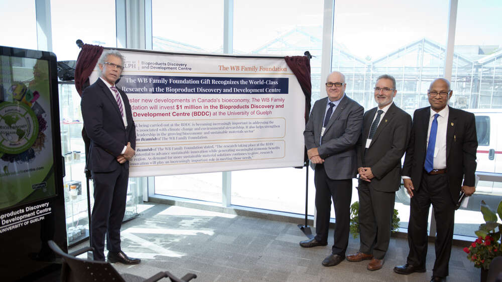 Four people in suits stand near a sign announcing a gift to the BDDC