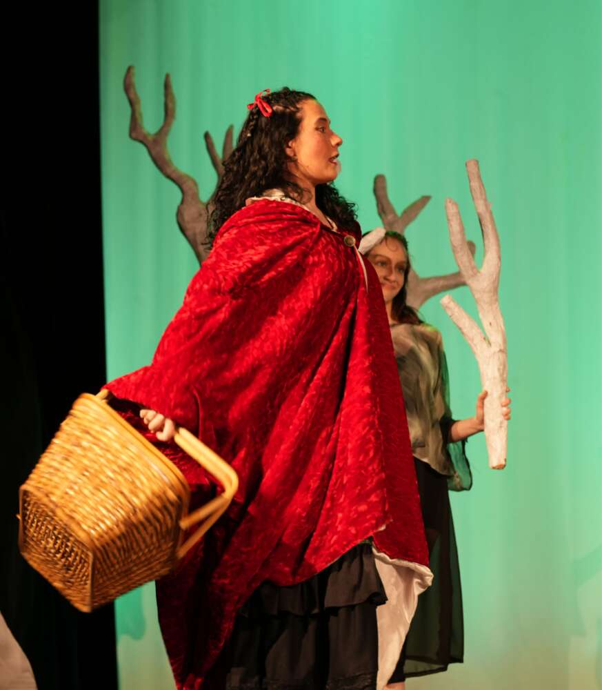 person in red cape holding basket performs on stage