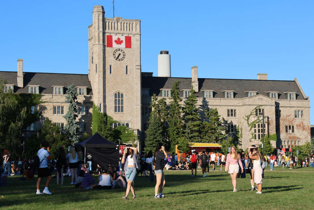 people walk across green lawn in front of tents and stone building