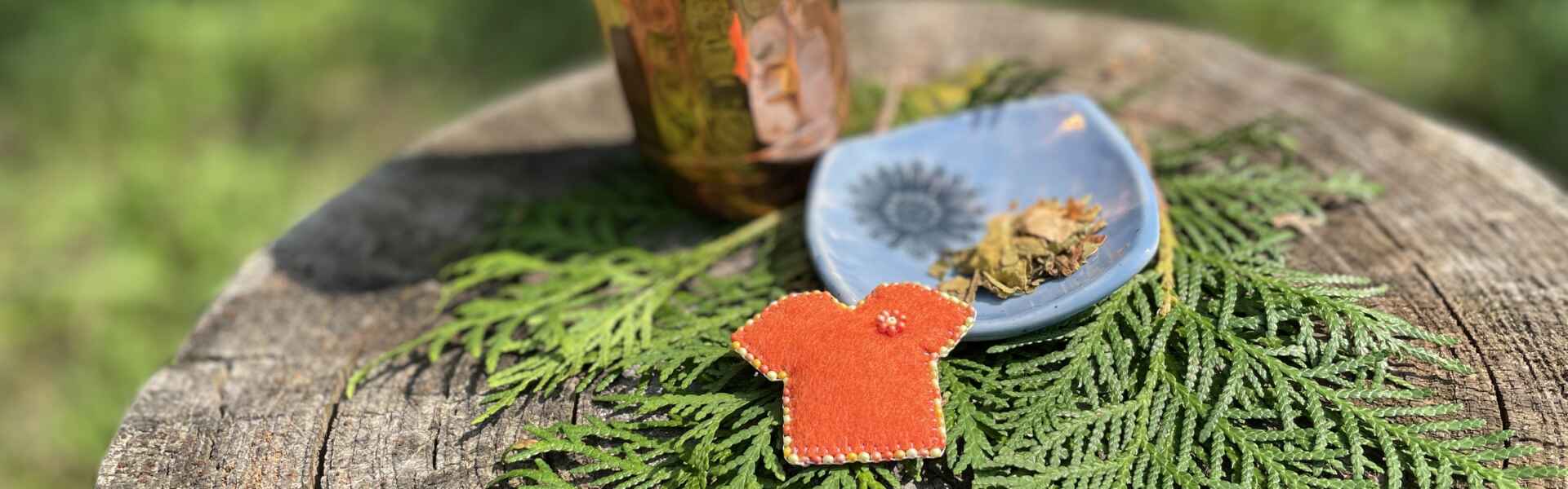 A tiny orange shirt next to some Indigenous medicines and a copper cup.