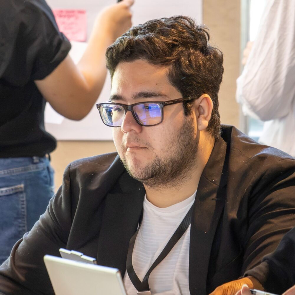 person in glasses sits at table in front of laptop