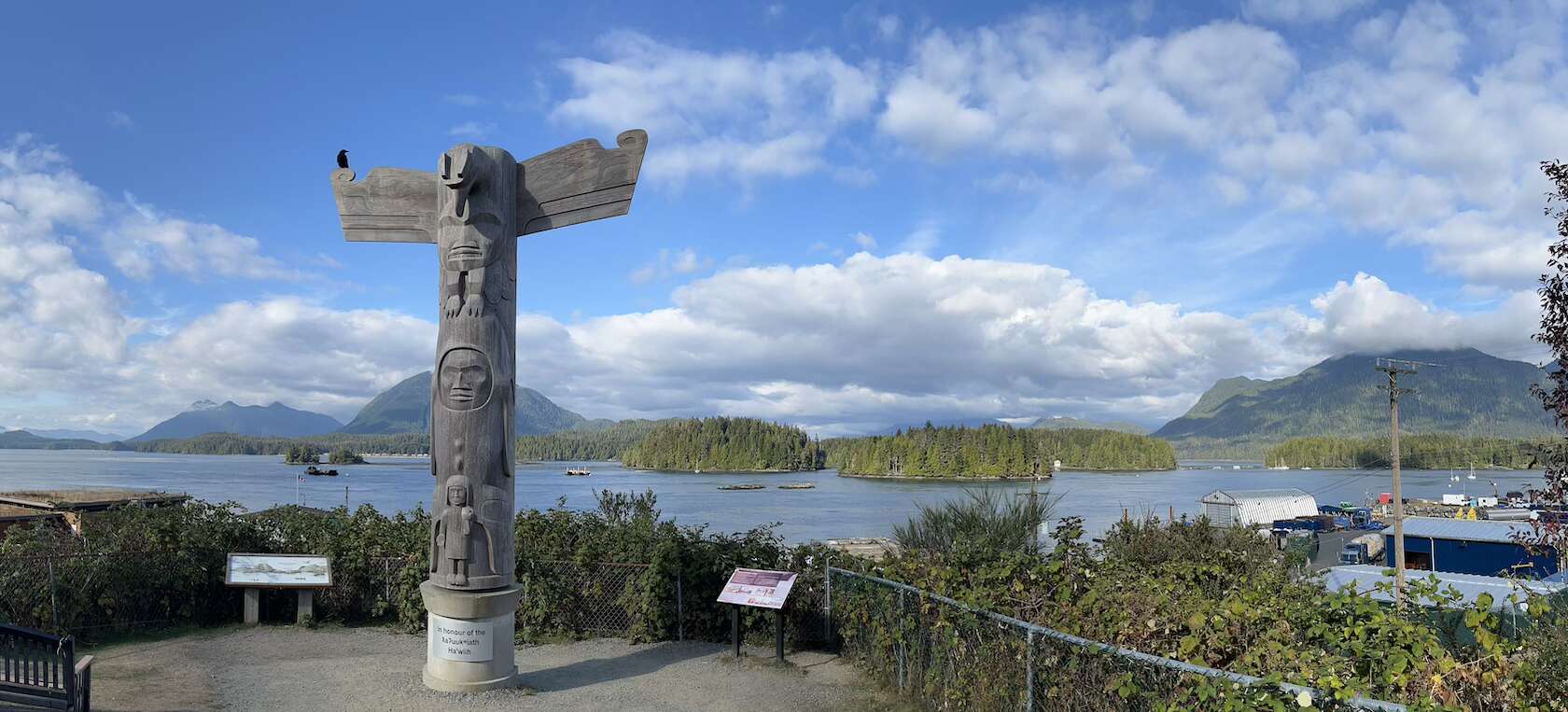A totem pole stands in downtown Tofino, B.C. against a backdrop of mountains, ocean and sky.