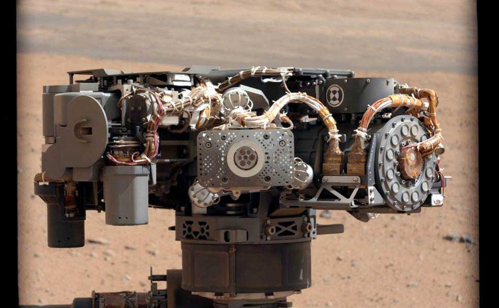 several instruments and wires on a rover arm, with Mars terrain in background