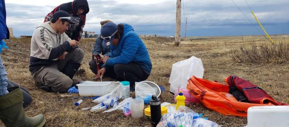 Several people kneel while looking at samples, surrounded by bags of sample bottles and other equipment
