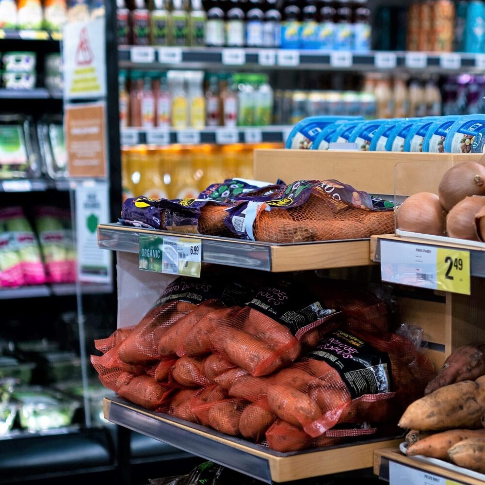 Onions and sweet potatoes are displayed in a grocery store produce area