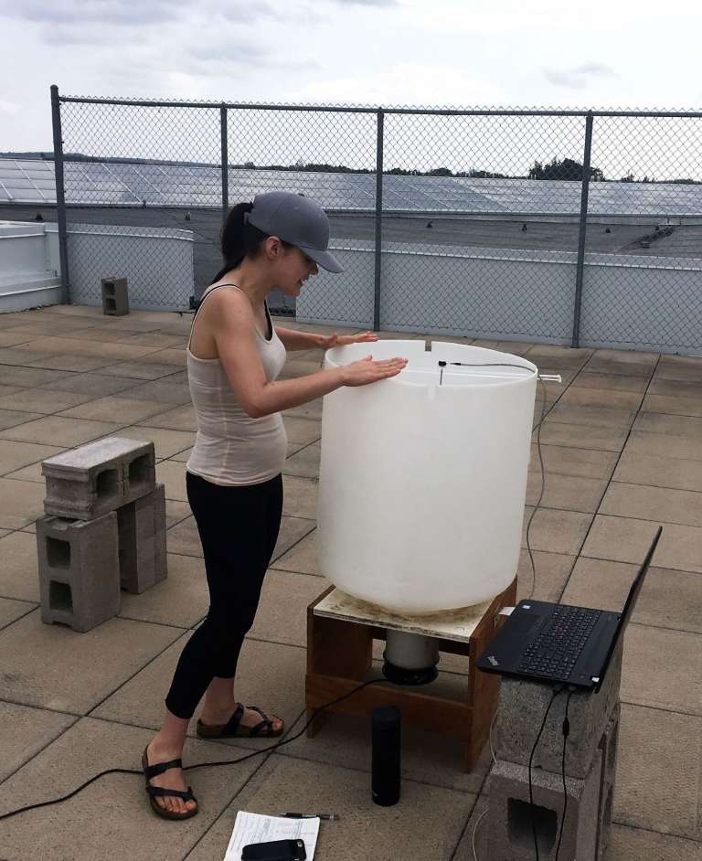 Alanna Wilcox stands on a rooftop and looks inside a large white plastic bin
