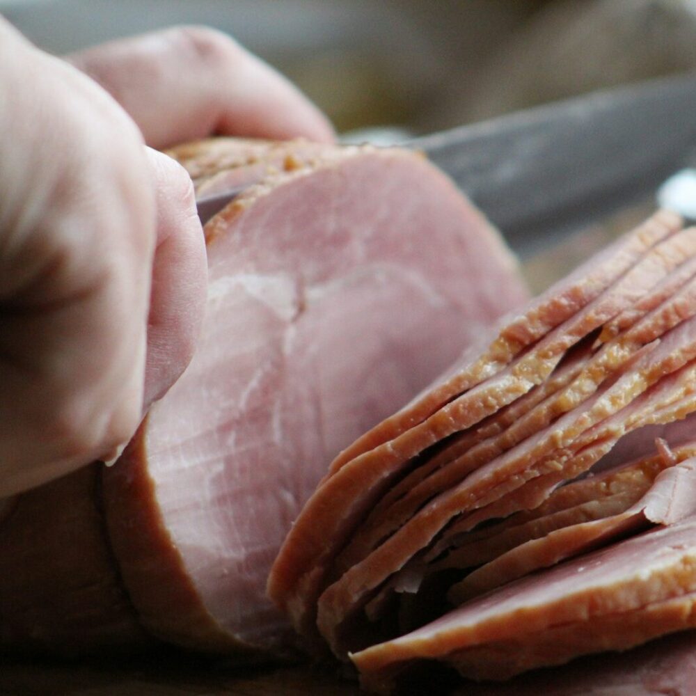 a person slicing ham on a cutting board