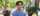 A person in a blue sweater stands smiling into the camera on a walkway surrounded by students and trees on U of G's campus.