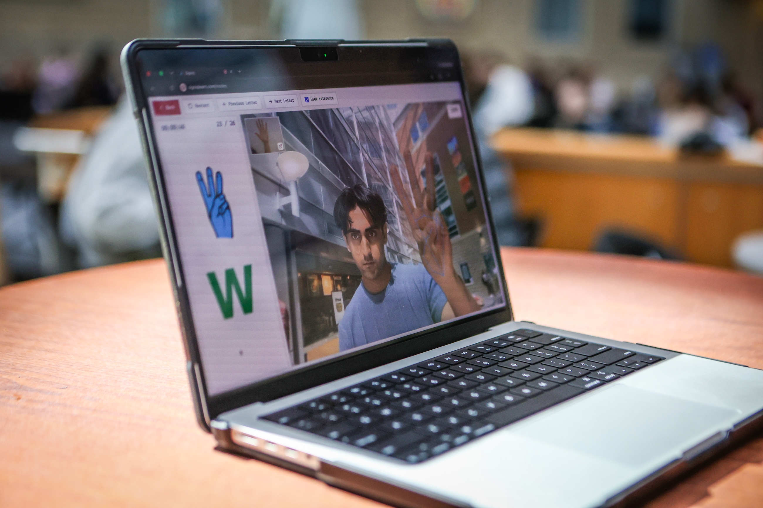 A laptop on a table shows the image of a person in camera view alongside text.