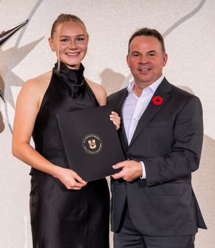 A person in a long, black gown is presented with an award that she holds beside a person in a gray suit and white shirt.
