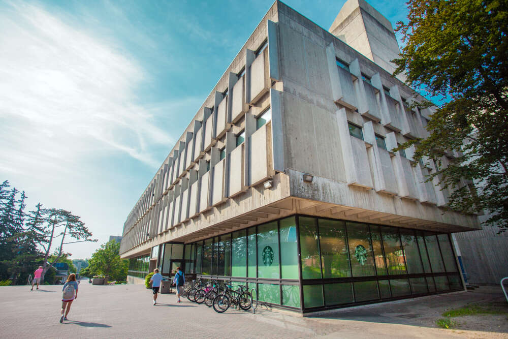 a large concrete building with students walking by with a green logo