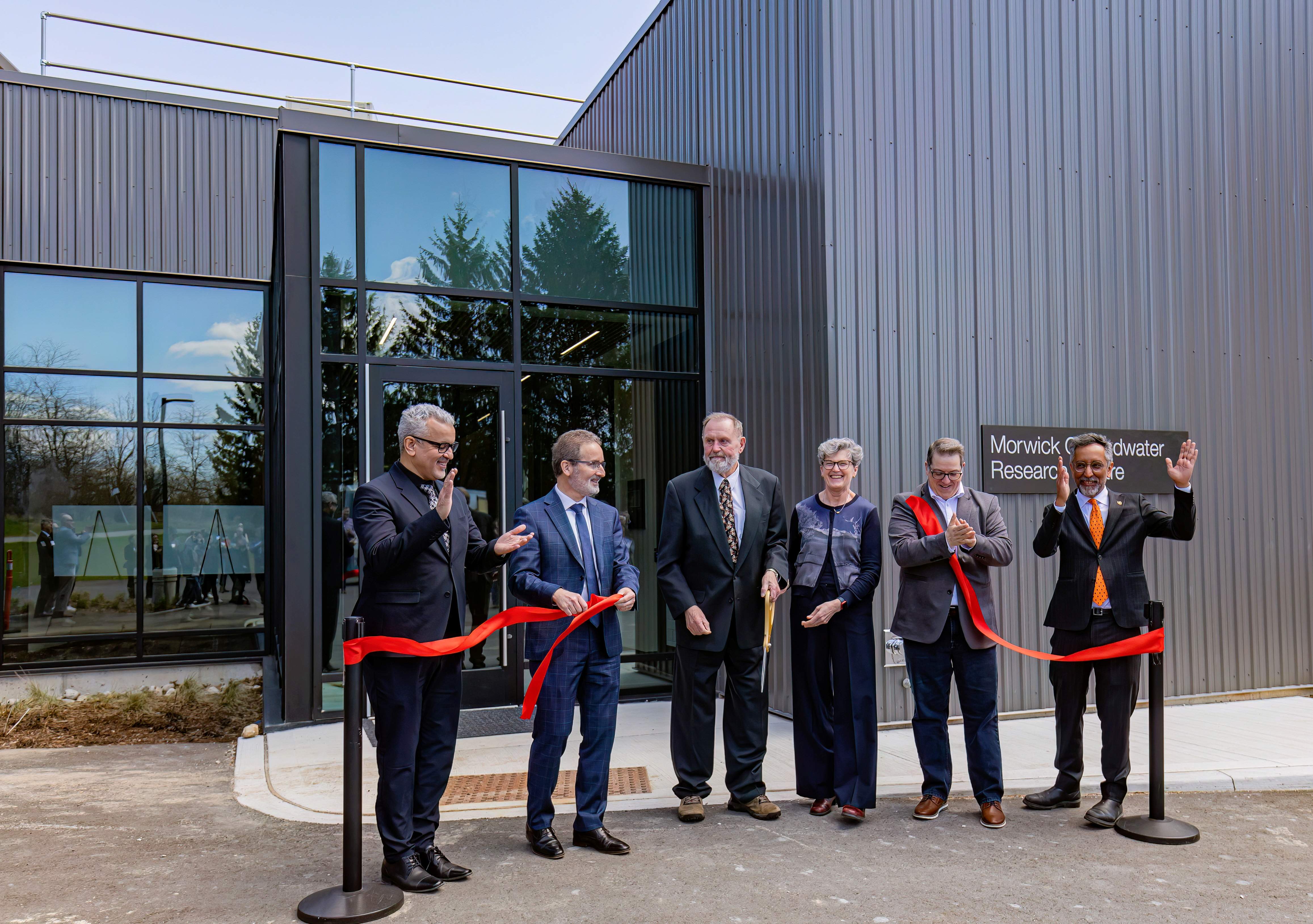 six people stand in front of a large ribbon and building